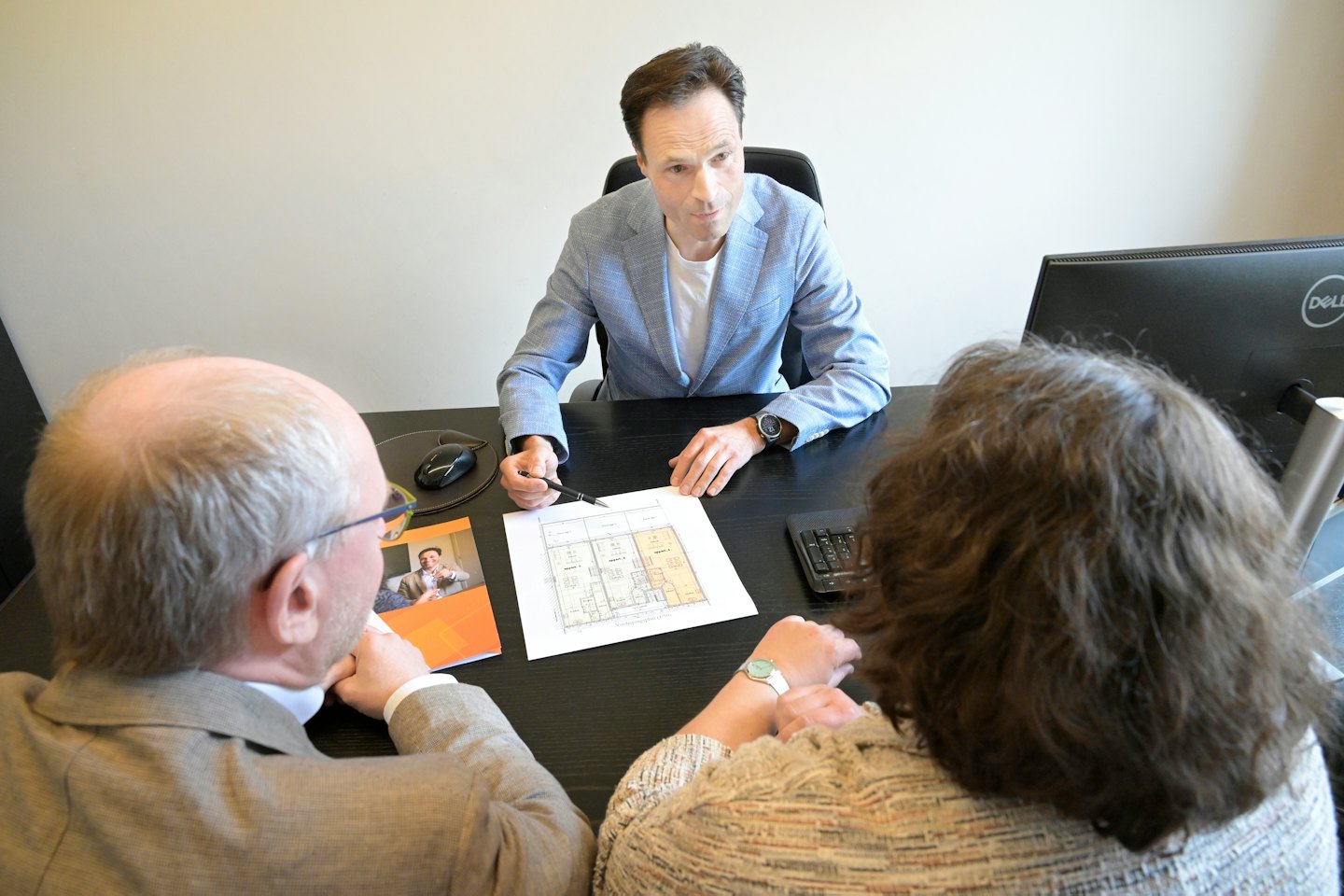 Man in blue blazer points to floor plan for a couple.